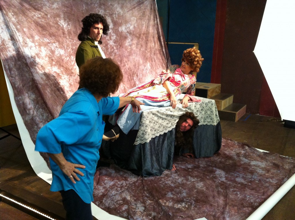 Joyce Maltby in blue directing Rob Duval as Tartuffe, Melinda Maltby as Elmire, and under the table, David Starr playing Orgon